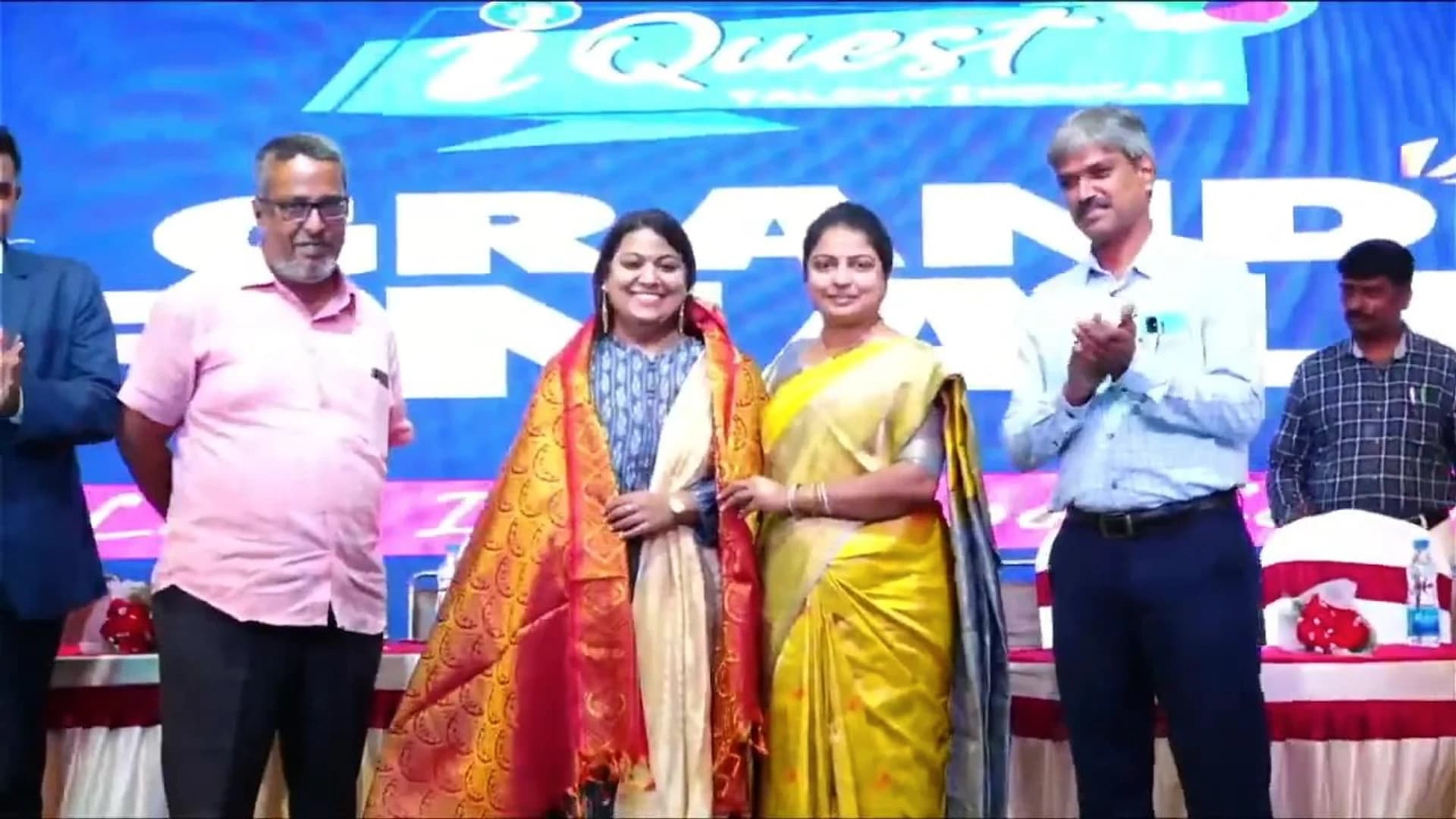 Pushpa Valli being honoured with a ceremonial shawl on stage at an iQuest event.